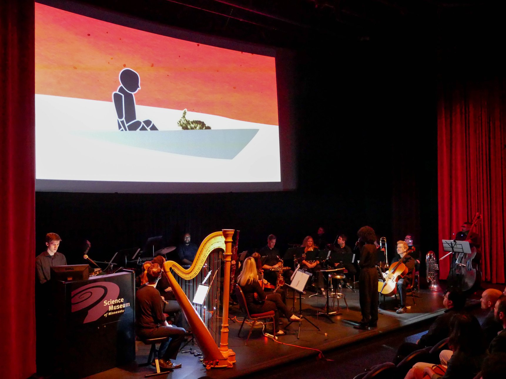 A theater stage with a group of musicians. A video is being projected behind them