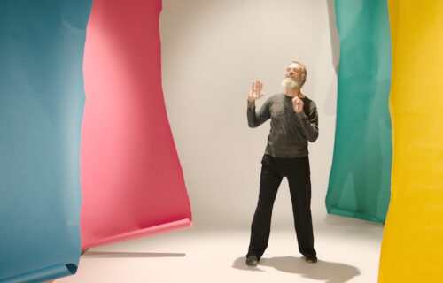 Patrick Scully dancing surrounded by large differently colored sheets of paper