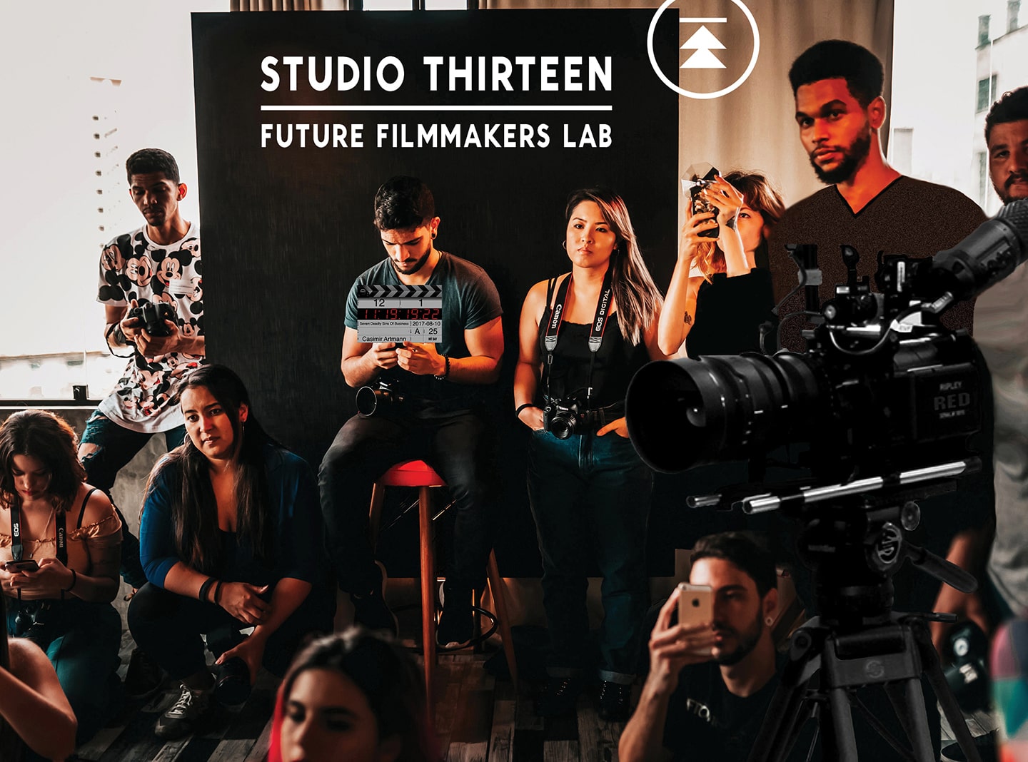 Group of young adults gathered. Some holding DSLRs and mobile phones. A sign in the background titled "Studio Thirteen, Future Filmmakers Lab"