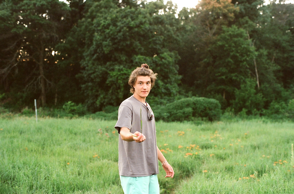 A young man standing in a field holding up a blade of grass
