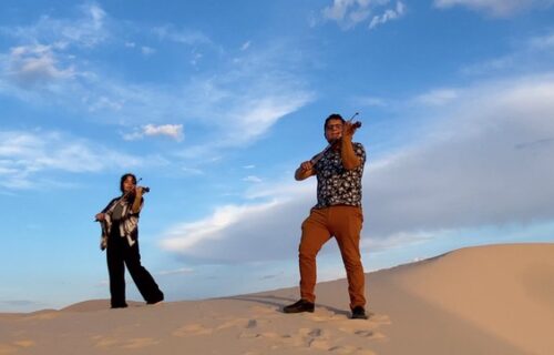 A man and woman playing violens in the desert